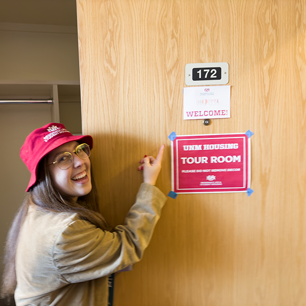 student in a red hat points to sign on door
