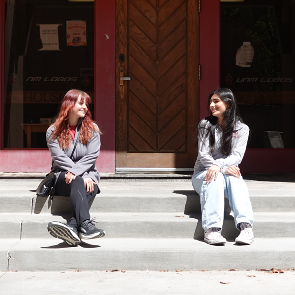 Photo of two students sitting in front of a doorway.