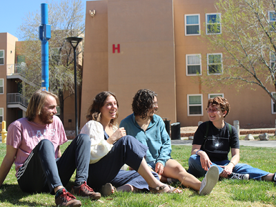 Four students sitting on the grass in front of Santa Clara Hall. SRC apartments in the background.